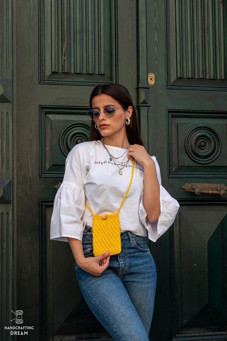 Puede incluir: Una mujer con una camiseta blanca con el texto "Good girls go to heaven, bad girls go everywhere" y pantalones vaqueros azules sostiene un bolso de hombro de crochet amarillo.