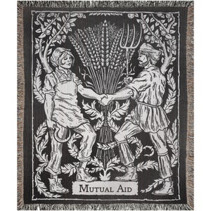 May include: Black and white woven throw blanket featuring a detailed illustration of two figures shaking hands, surrounded by wheat and foliage. The words "Mutual Aid" are at the bottom. The blanket has a fringed edge.