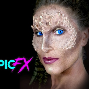 Peut inclure: Une femme avec des lentilles de contact bleues et un maquillage blanc sur le visage. Le maquillage est conçu pour ressembler à des écailles. La femme regarde la caméra. Le texte "EPIC FX" est dans le coin inférieur gauche de l'image.