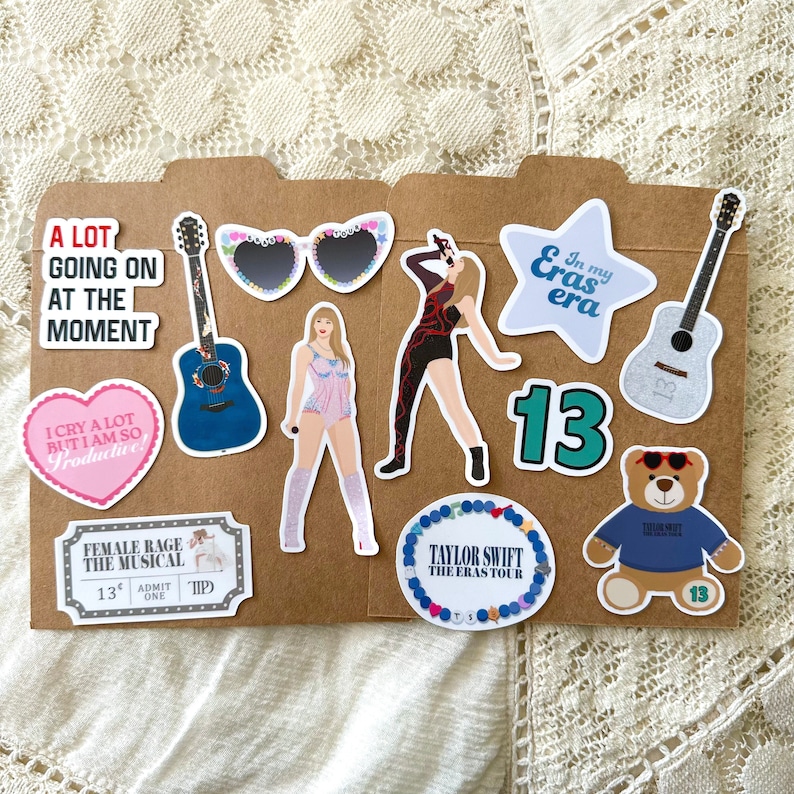May include: A collection of stickers featuring Taylor Swift themed designs. The stickers include a blue guitar, a pink heart with the text "I cry a lot but I am so productive", a pink ticket with the text "Female Rage The Musical", a blue and white guitar, a pair of sunglasses with pink and white hearts, a woman in a pink outfit, a woman in a black outfit, a blue star with the text "In my Eras era", a teal number 13, a blue bracelet with the text "Taylor Swift The Eras Tour", and a blue teddy bear with the text "Taylor Swift" and the number 13.