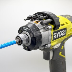 May include: A yellow and black Ryobi cordless drill with a blue screwdriver bit attached. The drill has a built-in LED light and a holder for multiple screwdriver bits.