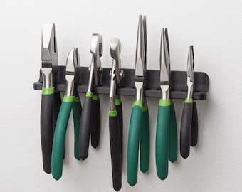 Può includere: Un supporto da parete nero per attrezzi che sostiene sette pinze in metallo con manici gommati neri e verdi. Il set include diversi tipi di pinze, come pinze a becchi lunghi, tronchesi e pinze universali, tutte appese in verticale.