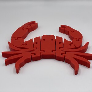 May include: A red plastic crab toy with segmented legs and claws. The crab is made of multiple pieces that fit together.