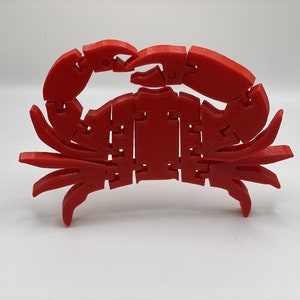 May include: A red 3D printed crab with segmented legs and claws. The crab is articulated and can be posed in different positions.
