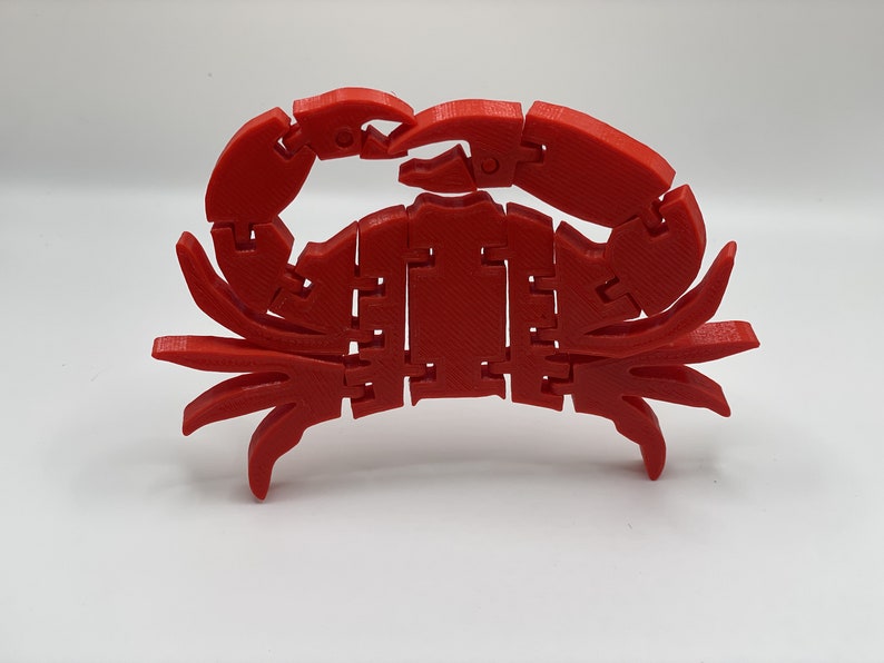 May include: A red 3D printed crab with segmented legs and claws. The crab is articulated and can be posed in different positions.