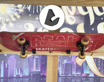 Könnte beinhalten: Ein rotes Skateboard mit schwarzen Achsen und Rädern ist mit schwarzen Metallhaken an einer Holzwand befestigt. Das Skateboard hat das Wort "REAL" in Weiß auf dem Deck aufgedruckt. Der Hintergrund ist ein verschwommenes Bild einer Skyline.