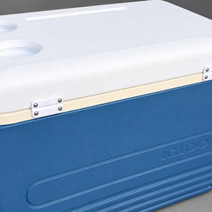 May include: A rectangular blue and white plastic cooler with a hinged lid. The lid features two circular cup holders and a long narrow slot. The word IGLOO is embossed on the front side of the blue base, which has horizontal ribbed detailing.