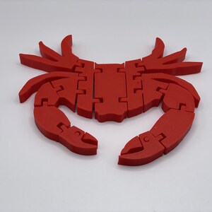 May include: A red plastic crab with segmented legs and claws. The crab is a 3D printed object and has a smooth, glossy finish.