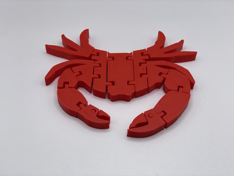 May include: A red plastic crab with segmented legs and claws. The crab is a 3D printed object and has a smooth, glossy finish.