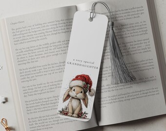 May include: A white rectangular paper bookmark featuring a brown bunny wearing a red Santa hat with holly berries. The text reads A VERY SPECIAL GRANDDAUGHTER. A silver metallic tassel is attached to the top through a small hole in the cardstock.