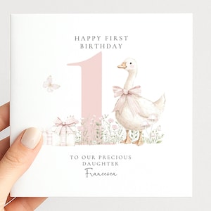 The image is a birthday card for a first-born daughter named Francesca. It features a white duck wearing a pink bow, surrounded by flowers and presents. The card has a pink background and the text "Happy first birthday" and "To our precious daughter Francesca" written on it.