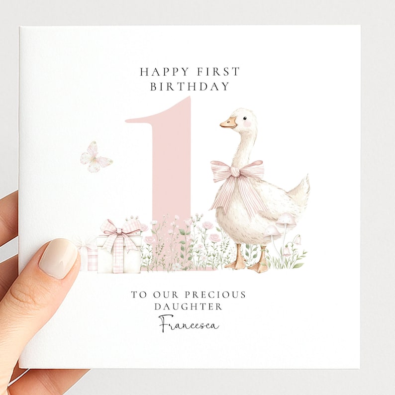 The image is a birthday card for a first-born daughter named Francesca. It features a white duck wearing a pink bow, surrounded by flowers and presents. The card has a pink background and the text "Happy first birthday" and "To our precious daughter Francesca" written on it.