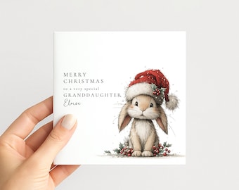 May include: A square greeting card featuring a tan bunny wearing a red Santa hat with white fur trim and holly berries. The text reads MERRY CHRISTMAS to a very special GRANDDAUGHTER Eloise. The bunny sits amidst red holly berries and green leaves.