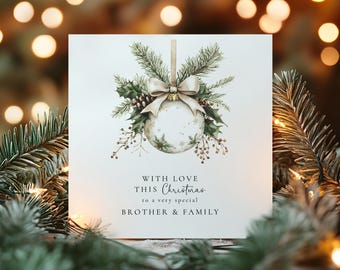 May include: A square white greeting card featuring a watercolor illustration of a Christmas ornament with a beige ribbon, pine branches, and holly. The text reads: WITH LOVE THIS Christmas to a very special BROTHER & FAMILY in black font.