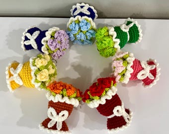 May include: A collection of handmade crochet flower bouquets in various colors, including blue, green, yellow, orange, red, pink, and purple. Each bouquet features a white ruffled collar and a white bow. These decorative items are likely keychains or small ornaments.