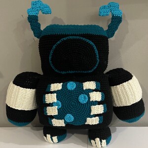 May include: A crocheted robot toy with black, white, and teal blue colors. The robot has two arms, two legs, and a round head with a teal blue face.