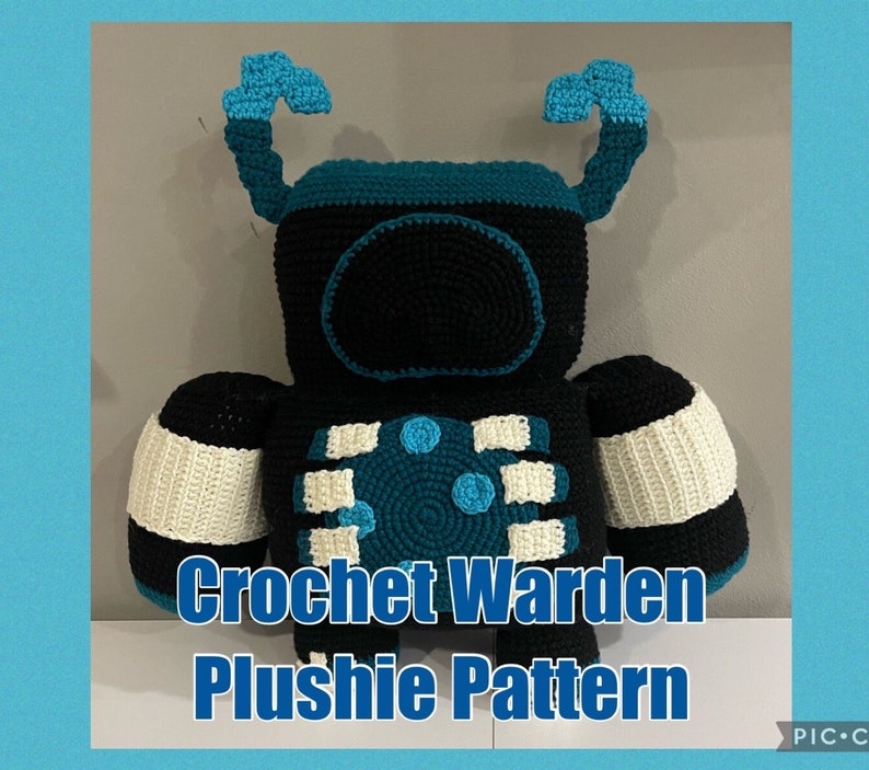 May include: Crochet Warden Plushie Pattern. A crocheted plush toy in the shape of a robot with black, white, teal, and blue yarn. The robot has a large head with a black face and teal antennas.