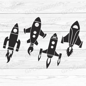May include: Four black silhouette rocket ship designs on a white wood background. The rockets are facing different directions and have different shapes.