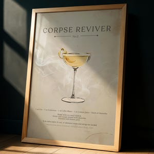 May include: A framed print featuring a cocktail recipe for a Corpse Reviver No. 2. The print has a light beige background with a drawing of the cocktail in a stemmed glass, garnished with a lemon peel. The text includes the recipe's ingredients and instructions.