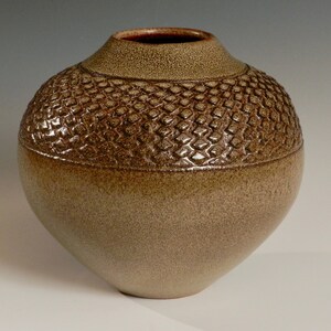 Könnte beinhalten: Eine Keramikvase mit einer strukturierten, braunen Glasur. Die Vase hat einen runden Körper und eine schmale Öffnung.
