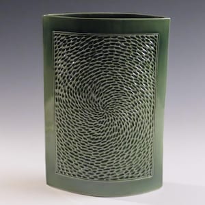 Könnte beinhalten: Eine hohe, grüne Keramikvase mit einem rechteckigen, strukturierten Design auf der Vorderseite. Der strukturierte Bereich weist ein Spiralmuster auf. Die Vase hat eine glatte, glänzende Oberfläche.