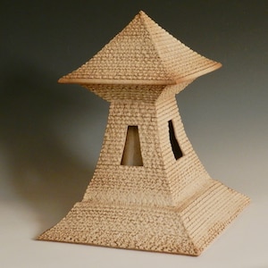 Könnte beinhalten: Eine Keramikskulptur eines Turms mit quadratischem Sockel und einem spitzen Dach. Der Turm ist aus hellbraunem Ton gefertigt und hat eine strukturierte Oberfläche. Der Turm hat zwei kleine Fenster an der Seite.