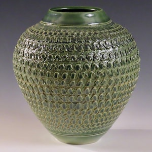 Könnte beinhalten: Eine grüne Keramikvase mit einer strukturierten Oberfläche. Die Vase hat einen runden Körper und eine breite Öffnung.