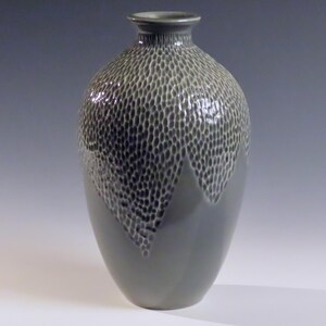 Könnte beinhalten: Eine graue Keramikvase mit einer strukturierten Oberfläche. Die Vase hat einen runden Körper und einen schmalen Hals.