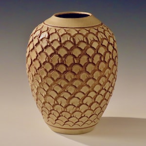 Könnte beinhalten: Eine Keramikvase mit hellbrauner Glasur und einer strukturierten Oberfläche, die an Schuppen erinnert. Die Vase ist rund und hat eine breite Öffnung.