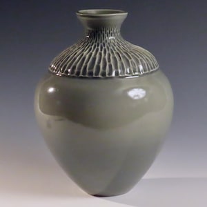 Könnte beinhalten: Eine graue Keramikvase mit einem strukturierten Rand und einer glatten, glänzenden Oberfläche.