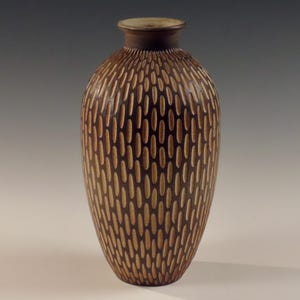 Könnte beinhalten: Eine braune Keramikvase mit einem strukturierten Muster aus hellbraunen Ovalen. Die Vase hat einen runden Körper und einen schmalen Hals.