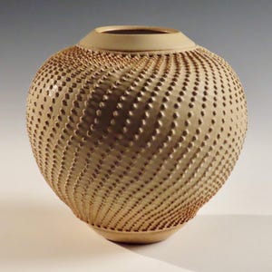 Könnte beinhalten: Eine beige Keramikvase mit einem strukturierten, spiralförmigen Muster aus kleinen erhabenen Punkten.