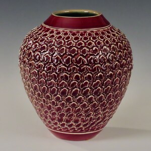 Puede incluir: Un jarrón de cerámica burdeos con un patrón texturizado en relieve de óvalos blancos. El jarrón tiene un cuerpo redondeado y un borde ligeramente acampanado.