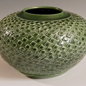Könnte beinhalten: Eine grüne Keramikvase mit einem strukturierten Diamantenmuster. Die Vase ist rund und hat eine breite Öffnung.