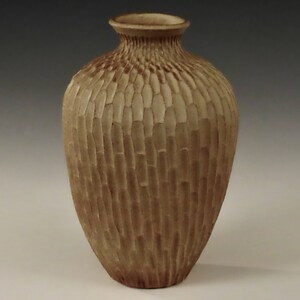 Könnte beinhalten: Eine Keramikvase mit einer strukturierten, hellbraunen Oberfläche. Die Vase hat einen runden Körper und einen schmalen Hals.