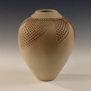 Könnte beinhalten: Eine hellbraune Keramikvase mit einem strukturierten Design. Die Vase hat einen runden Körper und einen schmalen Hals.