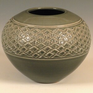Könnte beinhalten: Eine große, runde, grüne Keramikvase mit einem strukturierten, rautenförmigen Muster um die Mitte.