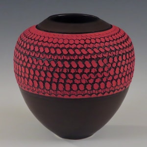 Könnte beinhalten: Eine dunkelbraune Keramikvase mit rotem Muster. Die Vase ist rund und hat eine breite Öffnung.