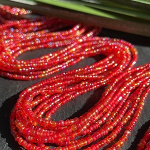 Könnte beinhalten: Nahaufnahme einer roten Perlenkette mit schillernden Perlen. Die Kette besteht aus mehreren Perlensträngen und ist aufgerollt.