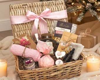 May include: A wicker gift basket with a pink bow, filled with spa products, sits in front of a decorated Christmas tree. The tree is adorned with pink and white ornaments and ribbons. Lit candles and wrapped gifts complete the festive scene.