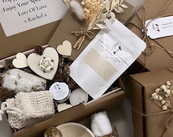 Könnte beinhalten: Eine braune Pappbox gefüllt mit einem Spa-Geschenkset. Die Box enthält weißes Badesalz, ein kleines Glas Lippenbalsam, eine weiße Kerze, ein Holzhäuschen mit einer weißen Blume, einen kleinen weißen Beutel, einen Holzlöffel, eine Schale mit getrockneten Blumen und ein weißes Handtuch. Die Box ist mit Schnur gebunden und hat einen Anhänger mit der Aufschrift "Ein besonderes Geschenk nur für dich".
