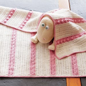 May include: A cream and pink crochet baby blanket with a matching stuffed sheep toy. The blanket features vertical pink stripes and a scalloped edge. The sheep has a cream body and large blue eyes.