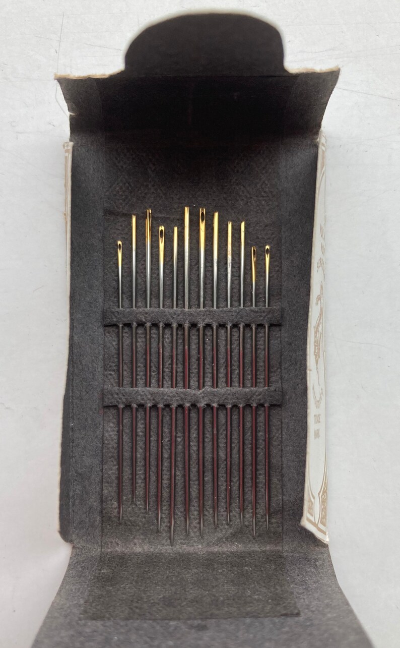 Op de afbeelding: Een doos met verschillende naalden, met een zwarte viltvoering en een wit label met gouden letters waarop "The Best Needles Made" staat.