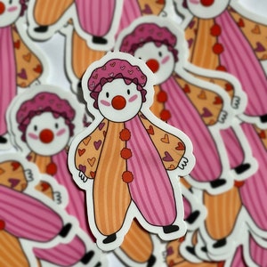 May include: A sticker of a cartoon clown with pink and orange striped clothing, a white face, and red nose. The clown has a pink and white heart pattern on their clothing.