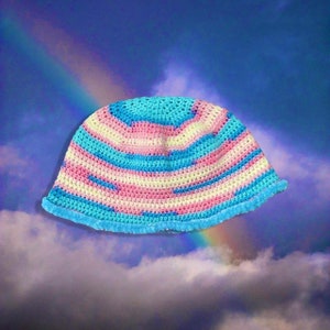 Könnte beinhalten: Ein gehäkelter Bucket-Hut mit einem gestreiften Muster in Blau, Rosa und Gelb. Der Hut hat einen flauschigen blauen Besatz am Rand.