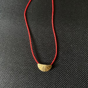 May include: A gold pendant with a sunburst design hangs on a red string necklace.