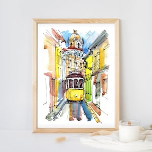 Puede incluir: Acuarela de un tranvía amarillo en una calle estrecha de Lisboa. La obra presenta edificios en tonos amarillos, naranjas y azules, con una cúpula de iglesia al fondo. La pintura está enmarcada en un marco de madera clara.