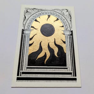 May include: A rectangular art print featuring a black and white ink illustration of a classical architectural archway with columns. Inside the arch, a central dark circle is surrounded by radiant gold leaf rays and black flame-like shapes.