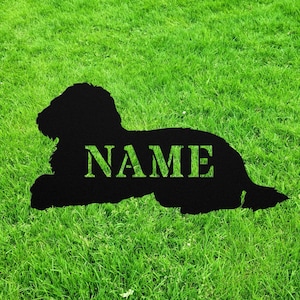 May include: Black metal silhouette of a dog lying down with the word "NAME" cut out of the silhouette. The silhouette is on a green grassy lawn.
