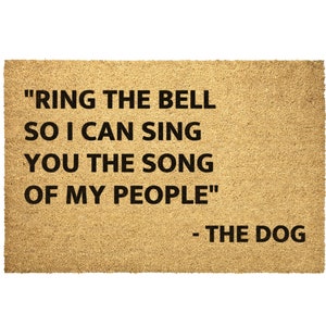May include: A brown doormat with the text "RING THE BELL SO I CAN SING YOU THE SONG OF MY PEOPLE" and "THE DOG" in black lettering.
